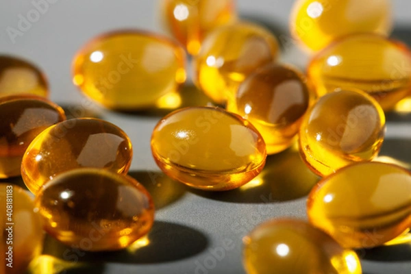 Fototapeta Yellow gelatin capsules on a gray background. Food supplement, vitamin D, omega, vitamin C, multivitamins. Soft focus
