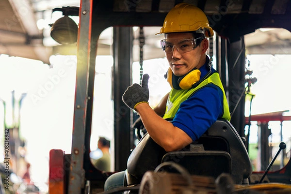 Fototapeta Engineer or technician Concept. A male employee driving a forklift and showing thumb up in factory.