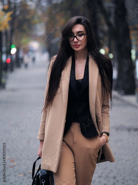 Fototapeta Brunette woman walking down the street in the park in a beige suit