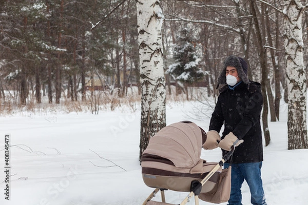 Fototapeta Father pushing baby stroller and walking at park in blizzard.