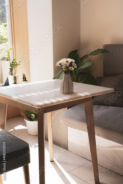 Obraz White flowers arranged in a ceramic vase, Was placed on a wooden table In the corner of the room where the sunshine was warm.