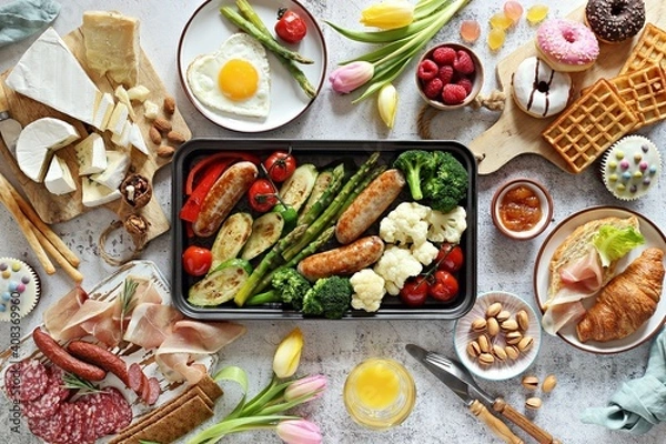 Fototapeta Breakfast food table. Festive brunch set, meal variety with grill platter, fried egg, croissant sandwich, cheese platter and desserts. Overhead view