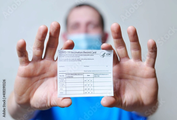 Fototapeta male is holding a vaccination record card and corona virus vaccine vials. Passport of immunity to the coronavirus in the hands of a male. Health passport as proof of recovery from COVID-19.
