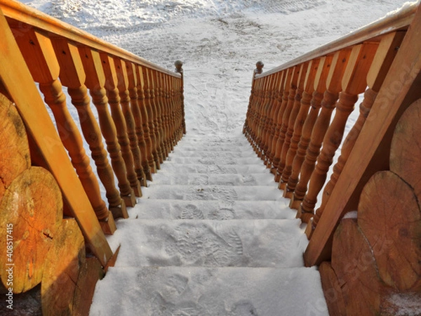 Fototapeta Snow-covered wooden stairs with carved handrails descend