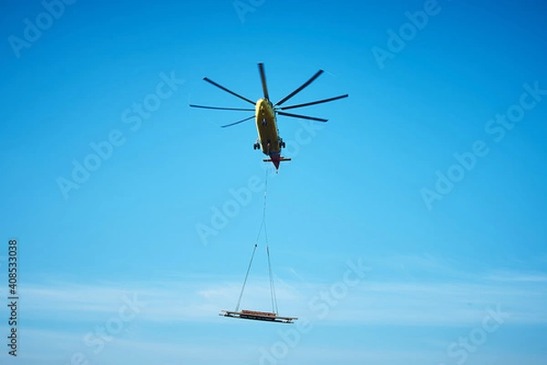 Fototapeta The world's largest cargo helicopter hovers overhead. Bottom view.The world's largest cargo helicopter transports cargo on a wire rope. Bottom view