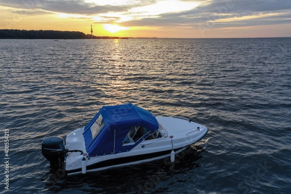 Obraz White pleasure boat against the setting sun on the Gulf of Finland on a summer day. Powerboat. Evening. Reflection of sun glare in the water.