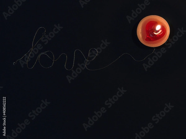 Fototapeta the inscription love inlaid with a silver chain on a black background and a candle flame