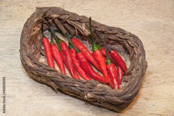 Fototapeta Red chili pepper on wicker basket on wooden background.
Top side view.