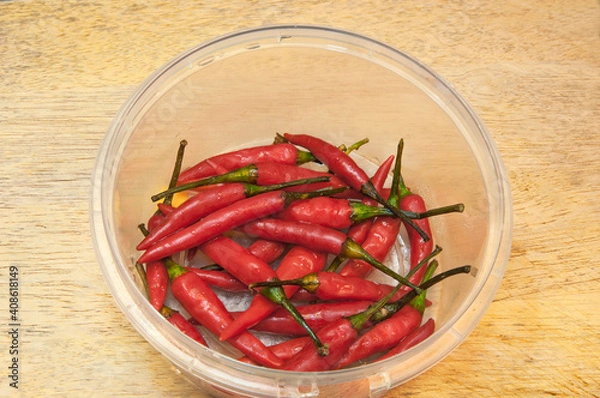 Fototapeta Red chili pepper in plastic container on a wooden background.
Top side view.