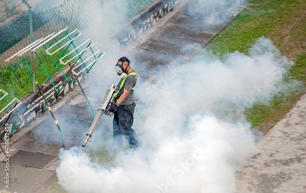 Fototapeta A worker fumigates to kill mosquito larvae to fight against the spread of dengue fever, Zika virus or Malaria at a residential area.