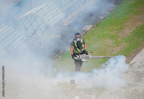 Fototapeta A worker fumigates to kill mosquito larvae to fight against the spread of dengue fever, Zika virus or Malaria at a residential area.