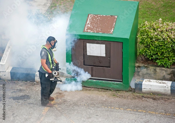Fototapeta A worker fumigates to kill mosquito larvae to fight against the spread of dengue fever, Zika virus or Malaria at a residential area.