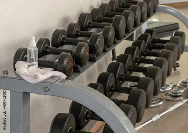 Fototapeta Cleaning exercise machines with alcohol sanitizer spray before lifting dumbbells in the gym or fitness. prevent Coronavirus infection,safety of the COVID-19 outbreak. Selective focus.