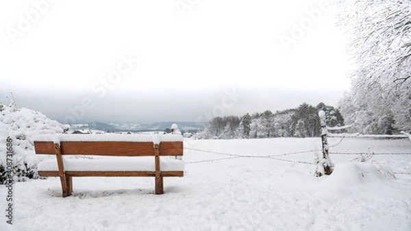 Obraz Verschneite Holzbank, im Hintergrund die weißen Ausläufer der Eifel