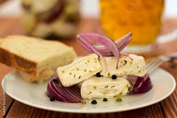 Fototapeta Camembert marinated in oil with red onion, spice and herbs. Presented on a white plate with bread.
