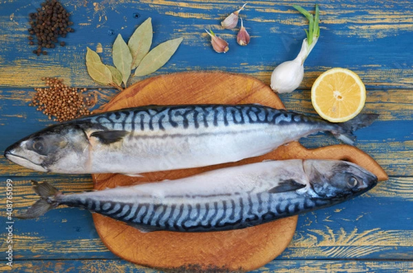 Fototapeta Two mackerel fishes on the wooden board ready for cooking decorated with lemon slices, spices on the blue wooden table. Top view
