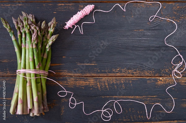 Fototapeta Fresh green asparagus bunch decorated with pink thread on the black wooden background. Top view with copy space