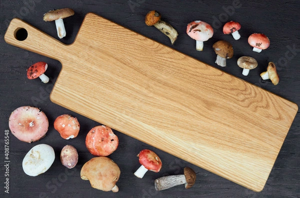 Fototapeta Empty wooden board decorated with wild edible various mushrooms on the black background. Top view with free copy space for text 