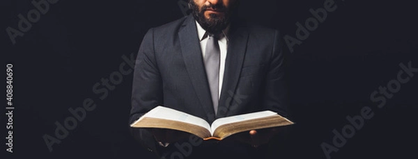 Fototapeta man in suit with an open bible on a black background
