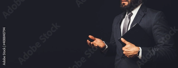 Fototapeta man in suit holding a bible in his arm speaking to another person on a black background