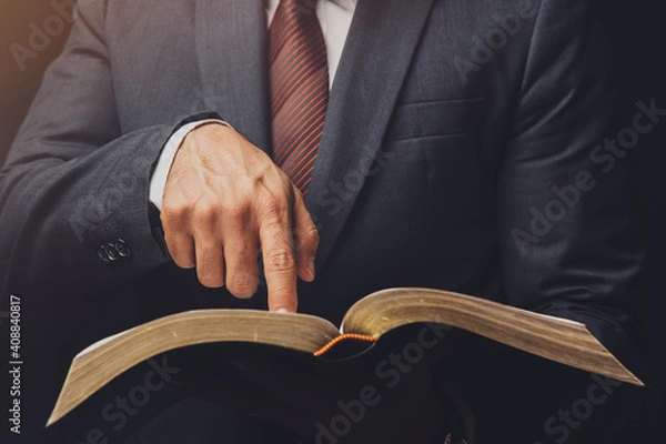 Fototapeta man in suit pointing a text on an open bible on a black background