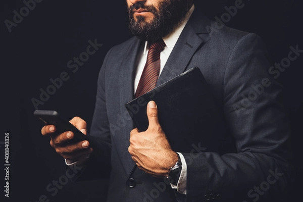 Fototapeta man in suit holding a bible in his arm and with the cell phone in hand
