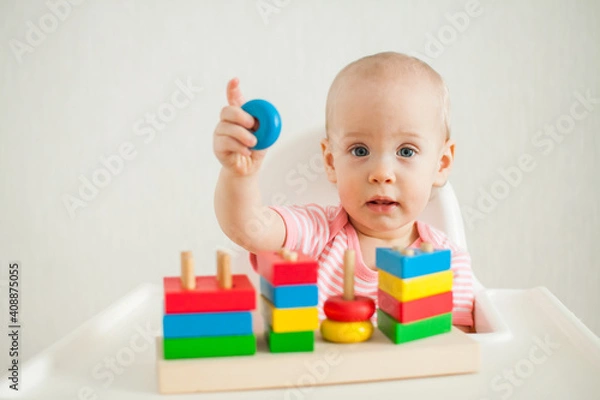 Fototapeta little girl plays with an educational toy - a multi-colored wooden pyramid. Development of fine motor skills and logical thinking. High quality photo
