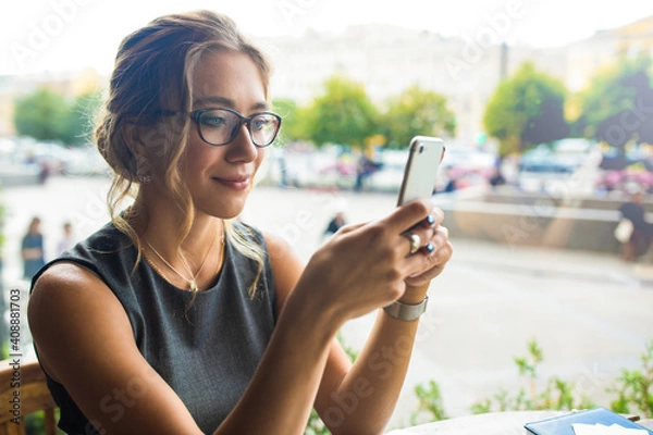 Obraz Beautiful female in glasses reading good news in e-mail on mobile phone while relaxing in restaurant