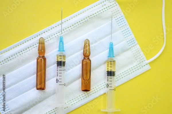 Fototapeta The concept of treatment and vaccination against coronavirus and other diseases. Medical face masks, syringes and ampoules on a yellow background. Flatley.