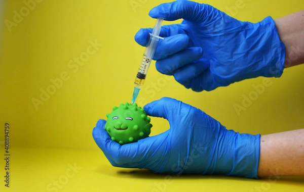 Fototapeta A woman wearing medical gloves gives an injection of the covid 19 coronavirus vaccine to a toy. A toy virus and a syringe on a yellow background. The medical concept of combating the covid-19 pandemic