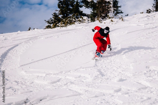 Fototapeta A guy in a red jumpsuit eating freeride on a snowboard on a snowy slope