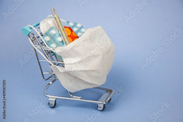 Obraz Shopping cart and medicine. An expensive medicine. Cough pills shopping basket with thermometer and medicine mask on blue background.