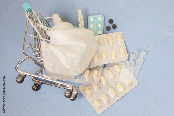 Obraz Shopping cart and medicine. An expensive medicine. Cough pills shopping basket with thermometer and medicine mask on blue background.
