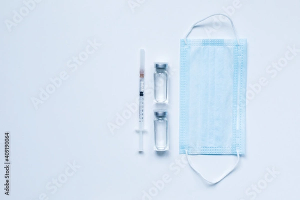 Fototapeta Two glass bottles with liquid , medical mask and syringe on gray background with copy space. The medical conception of combating the covid-19 pandemic. Flu vaccination.  Flat lay