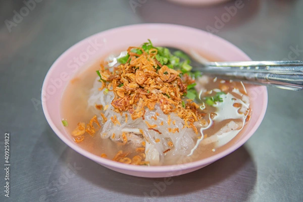 Fototapeta Vietnamese Rice Noodles Soup with pork spare ribs holding in fork and Vietnamese style sausage, deep fried red onion and parsley on wooden table background, popular delicious Vietnamese food