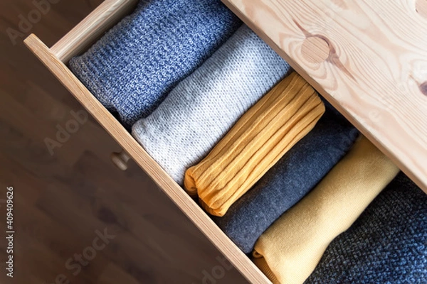 Fototapeta Open wooden dresser drawer with warm knitted woolen clothes. Home vertical storage. Wardrobe organizing.