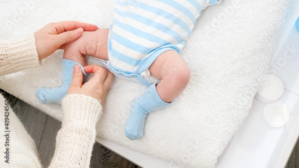 Fototapeta Closeup of young mother dressing her little baby son in socks while changing clothes on table. Concept of babies and newborn hygiene and healthcare. Caring parents with little children.