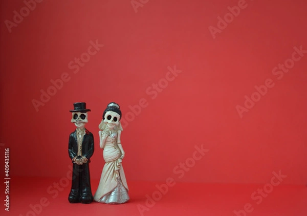 Fototapeta A close-up shot of two skeletons for Day of the Dead, Halloween, or Valentine's Day against a bright red background. Copy space