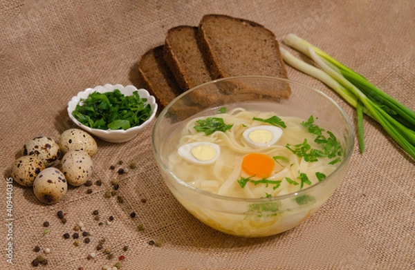 Fototapeta Broth with noodles eggs and herbs on burlap