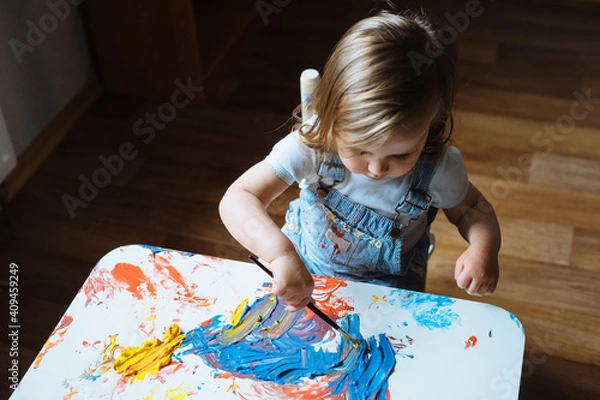 Fototapeta Child painting with paintbrush on the table at home