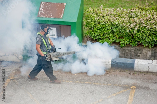 Fototapeta Healthcare worker using Fogging machine spraying chemical to eliminate mosquitoes and kill larvae to fight against the spread of dengue fever, Zika virus or Malaria at a residential area.