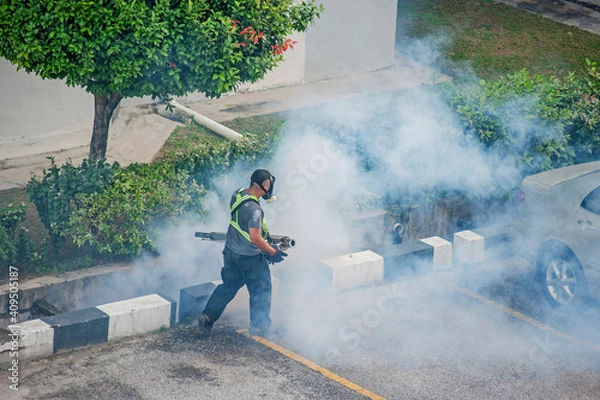Fototapeta Healthcare worker using Fogging machine spraying chemical to eliminate mosquitoes and kill larvae to fight against the spread of dengue fever, Zika virus or Malaria at a residential area.