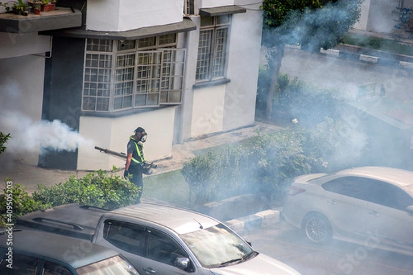 Fototapeta Healthcare worker using Fogging machine spraying chemical to eliminate mosquitoes and kill larvae to fight against the spread of dengue fever, Zika virus or Malaria at a residential area.