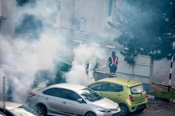 Fototapeta Healthcare worker using Fogging machine spraying chemical to eliminate mosquitoes and kill larvae to fight against the spread of dengue fever, Zika virus or Malaria at a residential area.