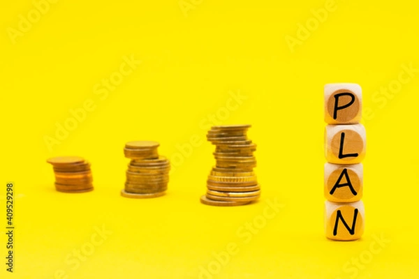 Fototapeta wooden cube with the word PLAN on yellow background stacks of coins. Business concept. .Business motivation,inspiration concepts ideas