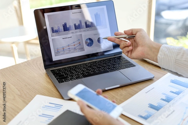 Fototapeta Management is checking laptop and mobile phone data for accuracy. He's looking at the company's annual income data in his office. Business management concept.