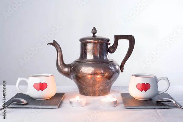 Fototapeta Teapot and two cups with painted hearts and burning candles.. Romantic tea time or breakfast. Concept of love and Valentines day   