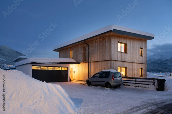 Obraz View of single-family house with garage in snow-covered winter with cleared entrance at night