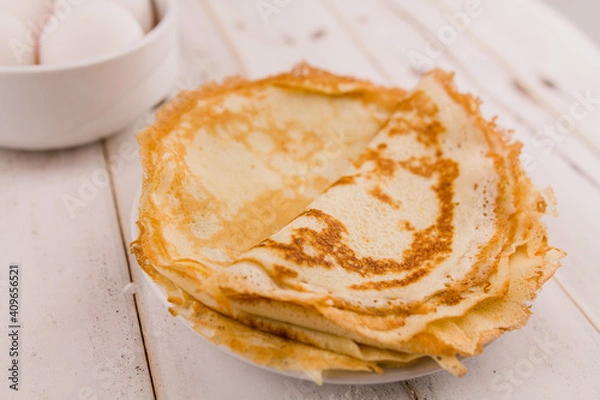 Fototapeta thin delicious round pancakes on a white plate on a wooden table in the kitchen with eggs and flour