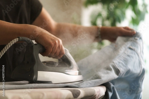 Fototapeta Primer plano de mujer ama de casa planchando los vaqueros con vapor en el salón de su hogar.
